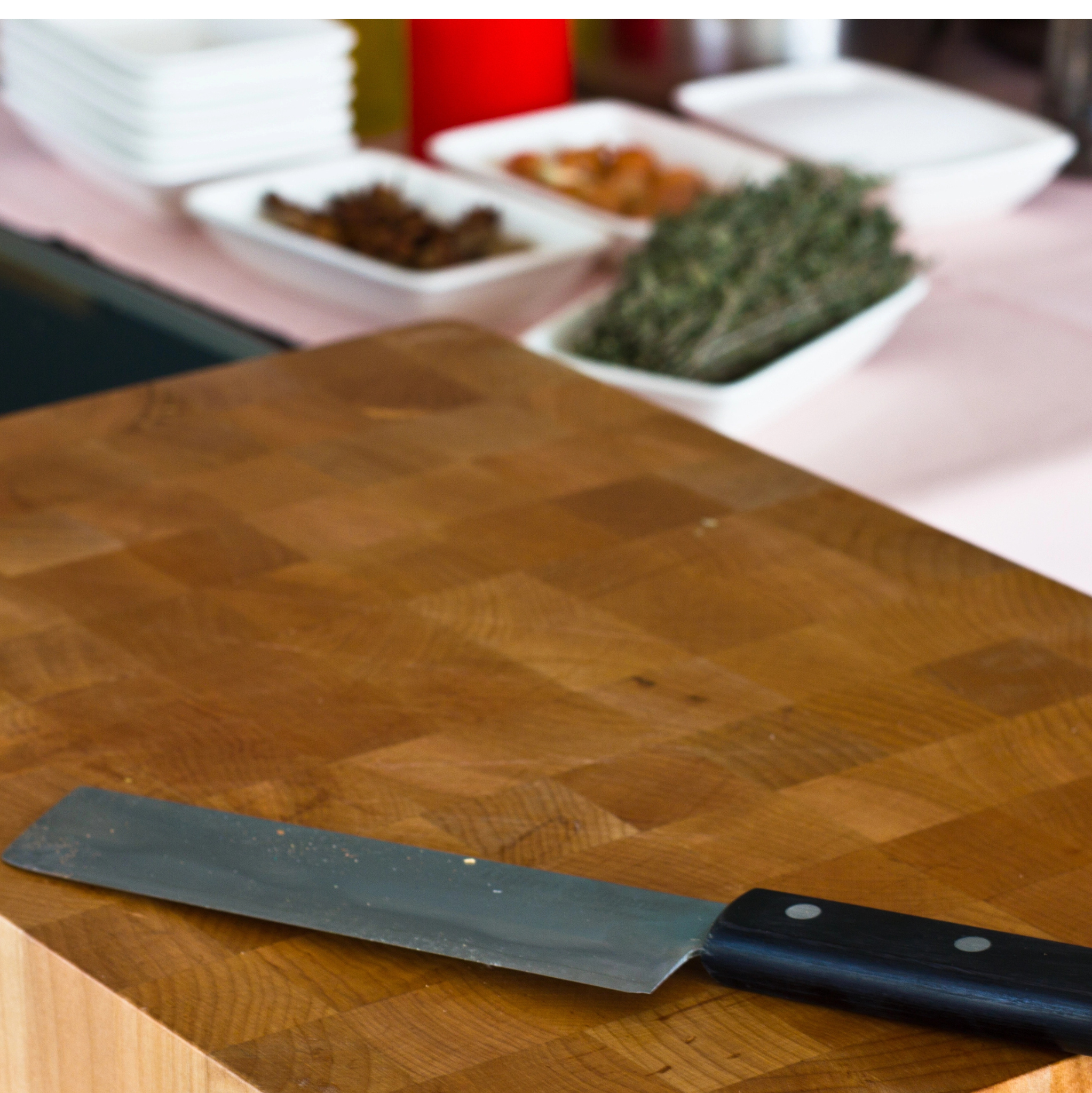 Butcher block table for cuting with kitchen visible and herbs in dishes.