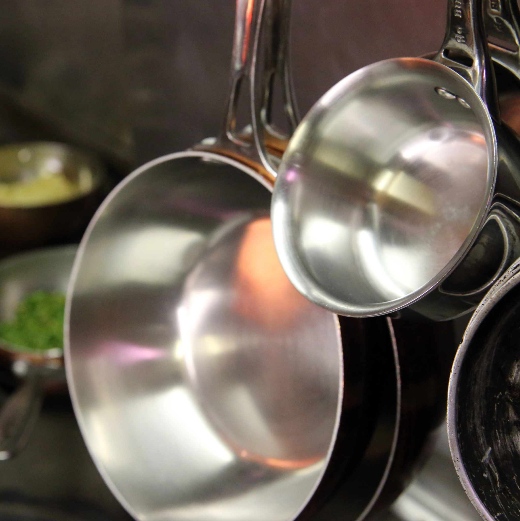 Stainless Pots hanging on pot rack with copper pots on stove below.